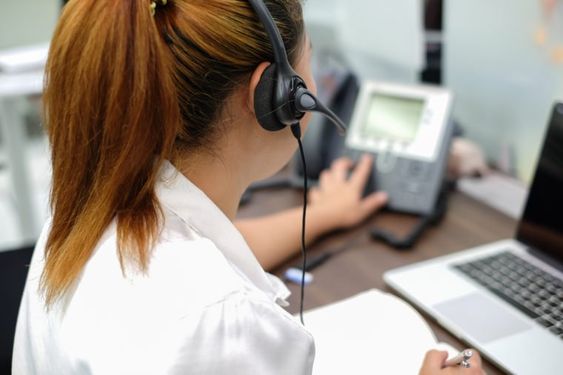 Mulher em escritório apertando botão de aparelho telefônico para as gravações das chamadas